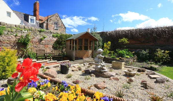 A stunning rockery in the garden with a summer house and bright flowers