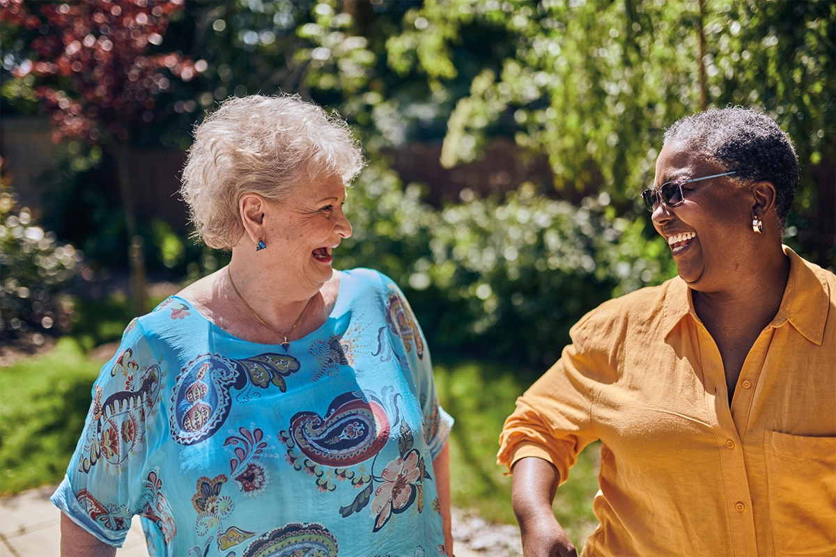 Two Older Women Laughing Together In Sunny Garden