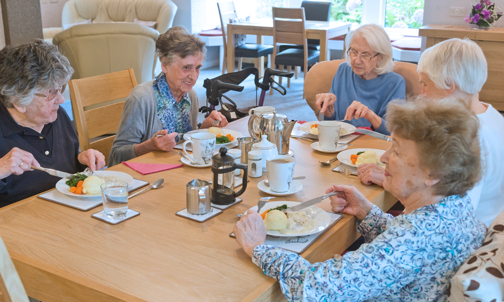 Five residents are sat around a table enjoying dinner