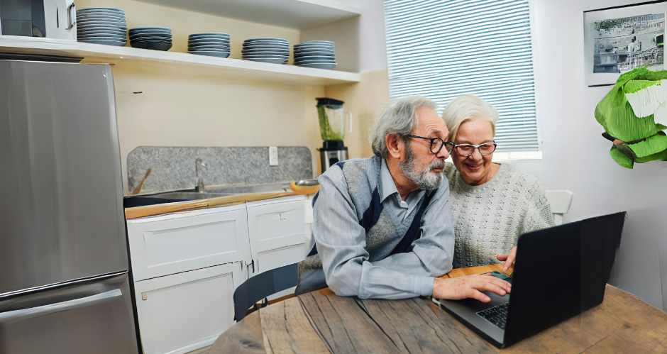 Older Couple Looking At Laptop Together On Kitchen Table