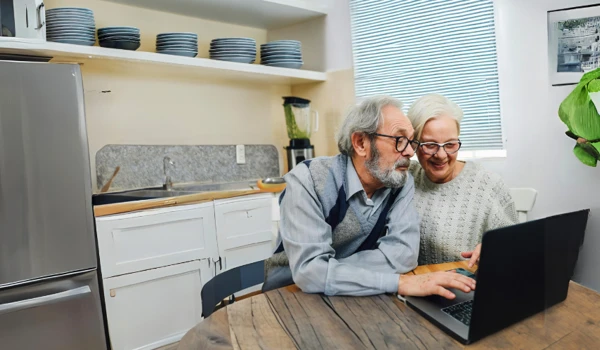 Older Couple Looking At Laptop Together On Kitchen Table