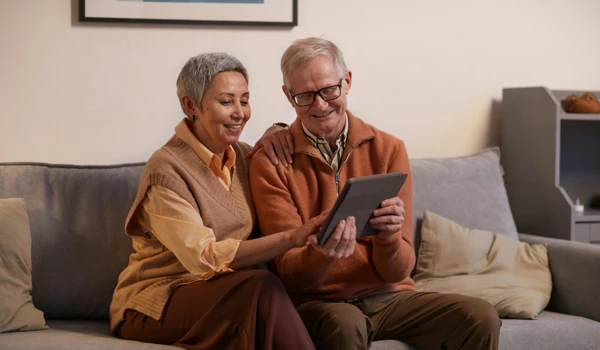 Older Couple Sitting On Sofa Looking At Tablet