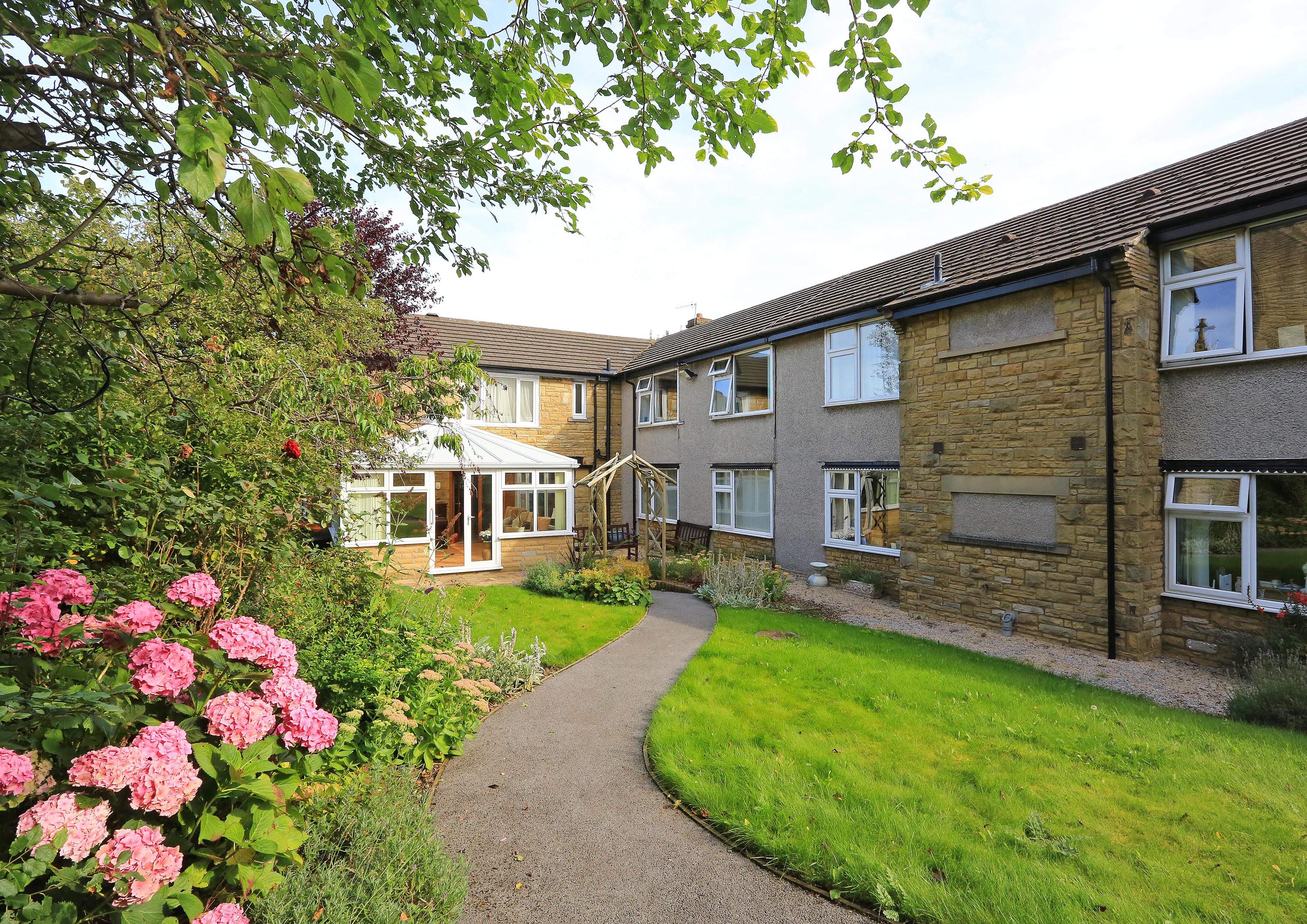 A path leading to the front of the house through flowers and trees