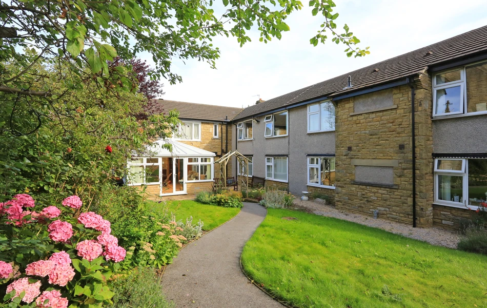 A path leading to the front of the house through flowers and trees