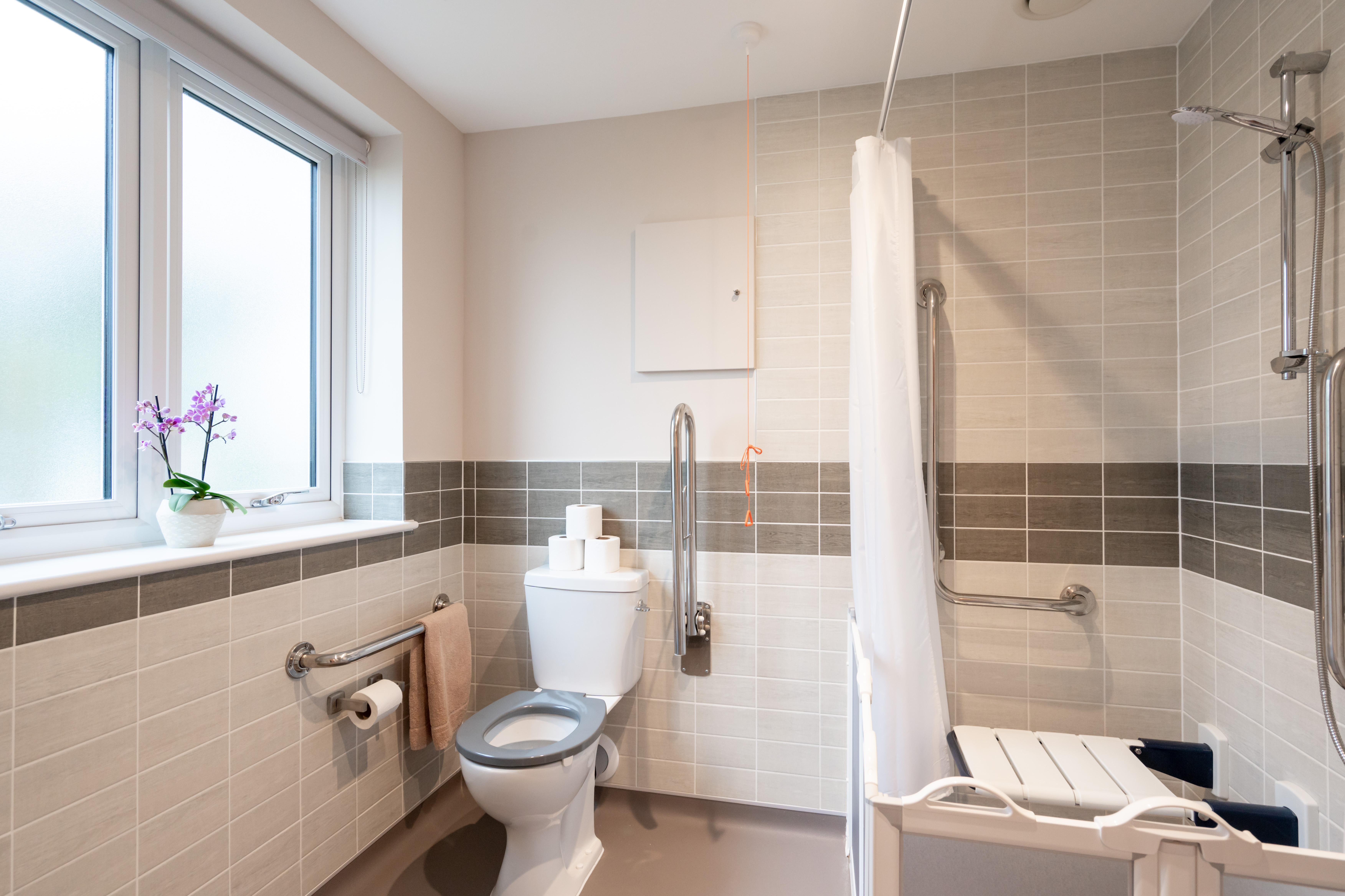 Bathroom at Westall House in Horsted Keynes with accessible features including grab rails, a raised toilet seat, and a walk-in shower with a seat.
