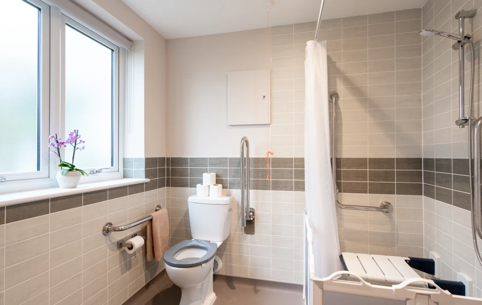 Bathroom at Westall House in Horsted Keynes with accessible features including grab rails, a raised toilet seat, and a walk-in shower with a seat.