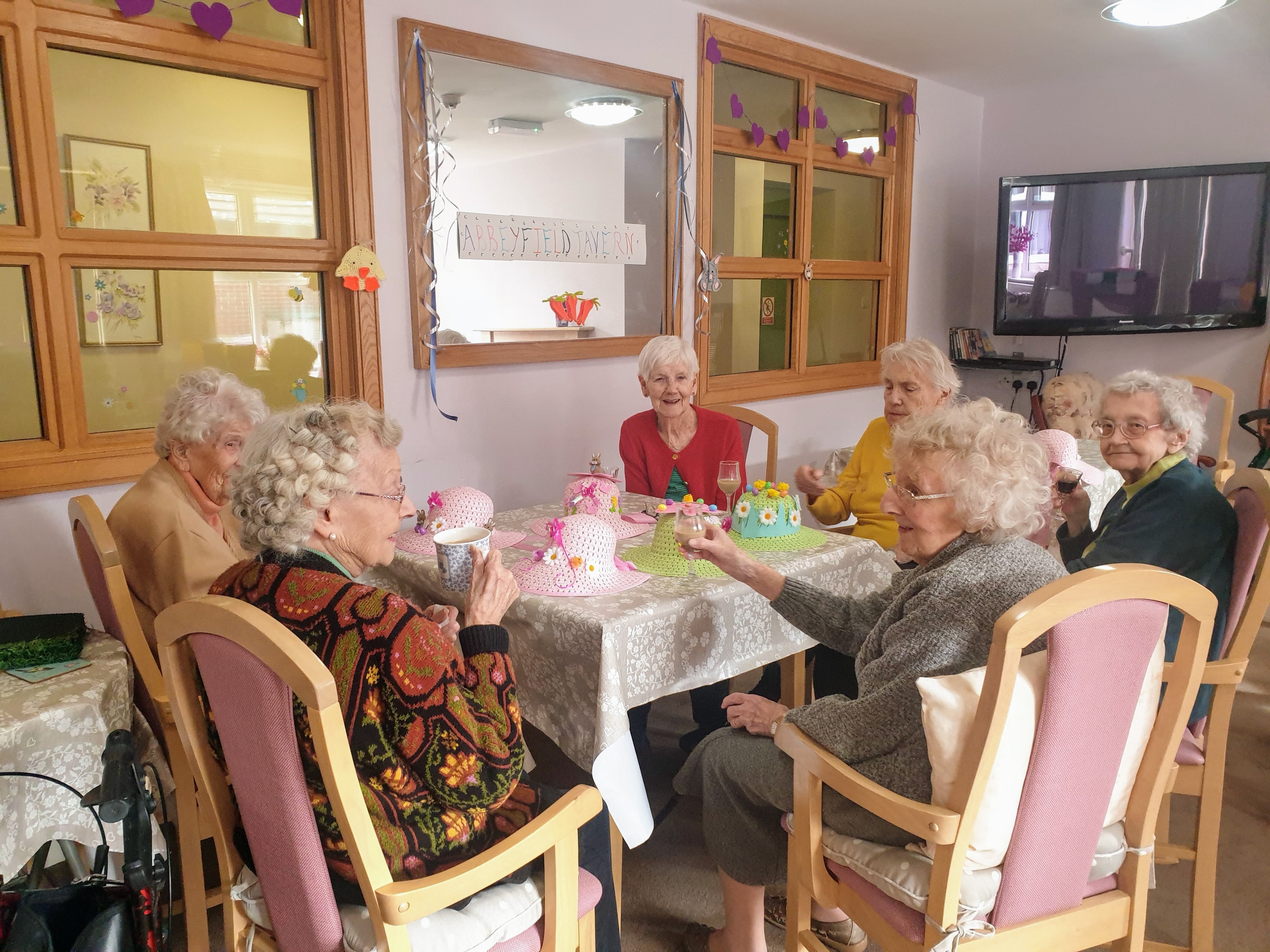 A group of residents sit around a dining table smiling and having a drink