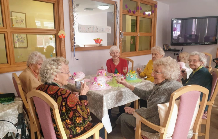 A group of residents sit around a dining table smiling and having a drink