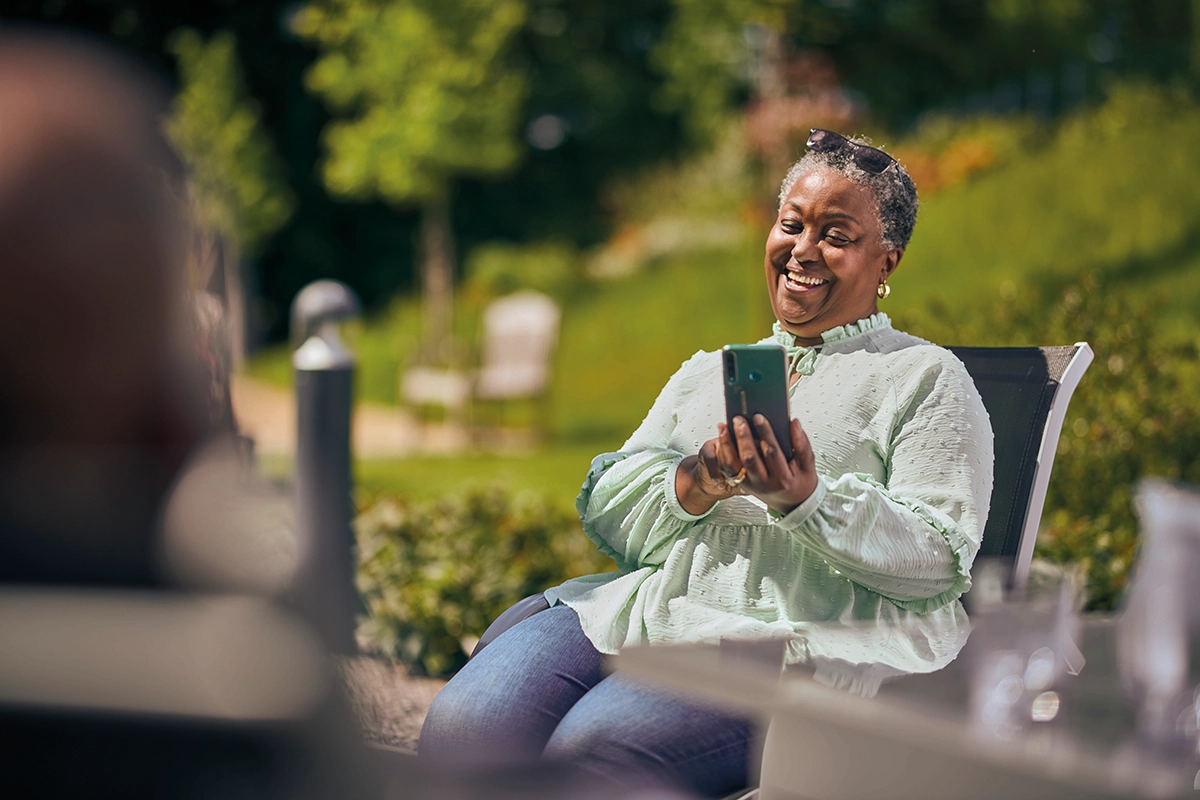 Older Woman Sitting On Bench In Garden Whilst Chatting On Phone