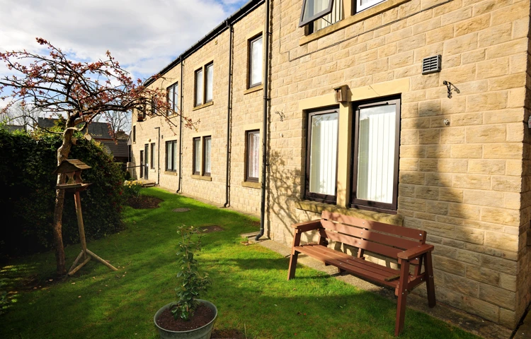 View of the side of the house with a garden bench and plant pot outside Abbeyfield House, Pudsey