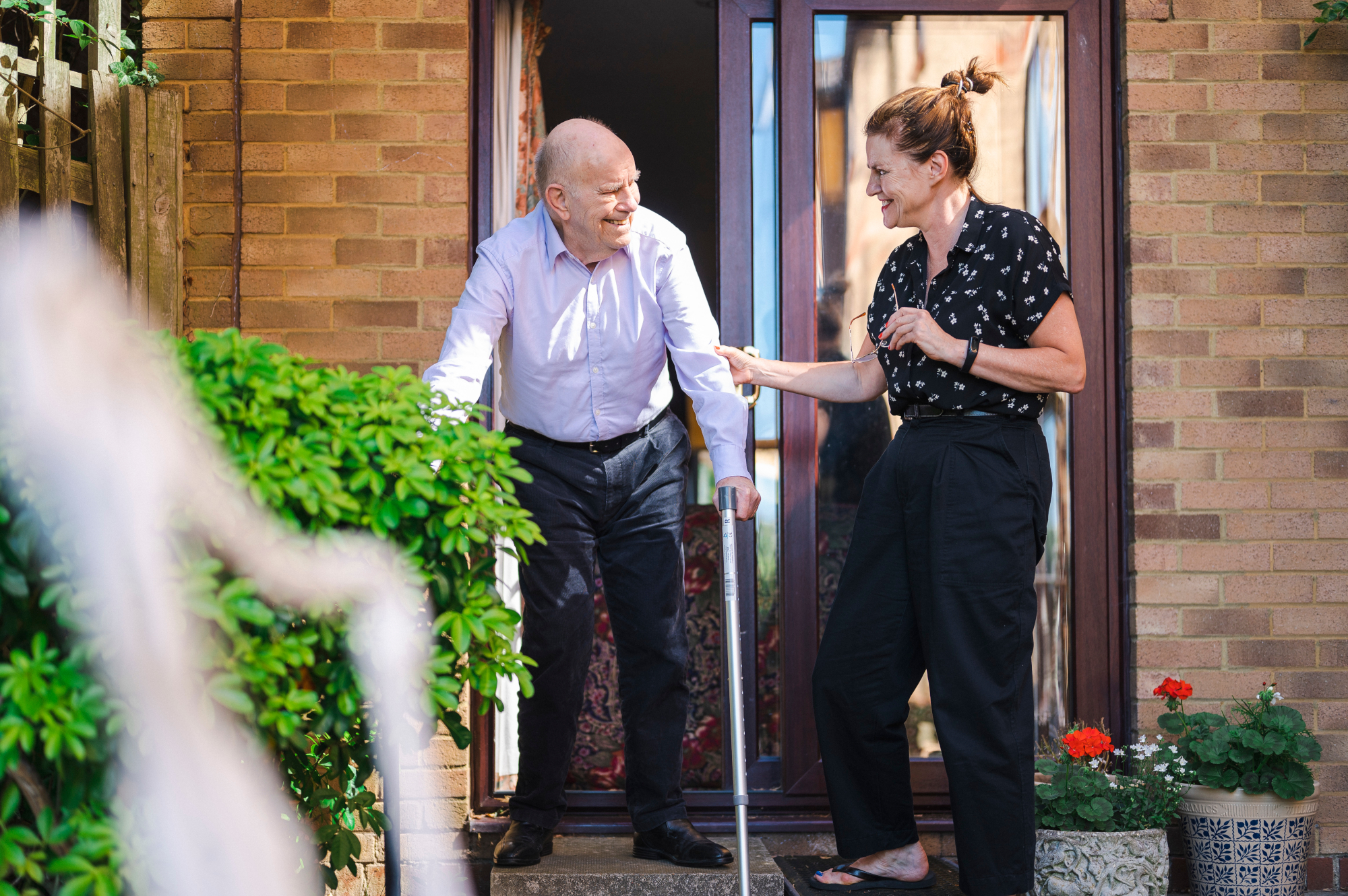 Woman Helping Older Man Outside Into The Sunshine