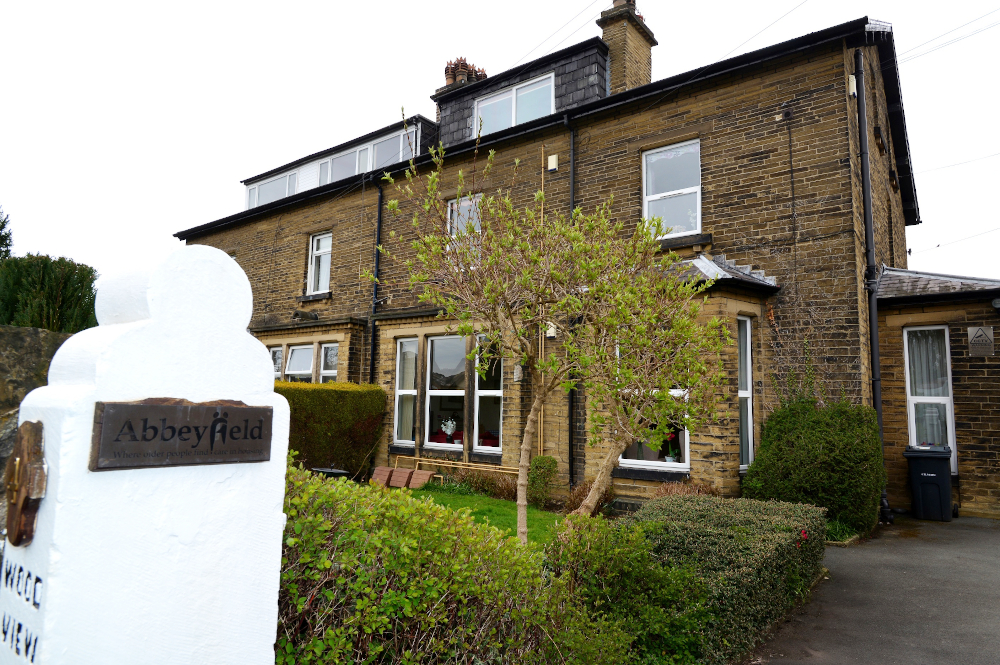 A white post with an Abbeyfield sign and the house in the background