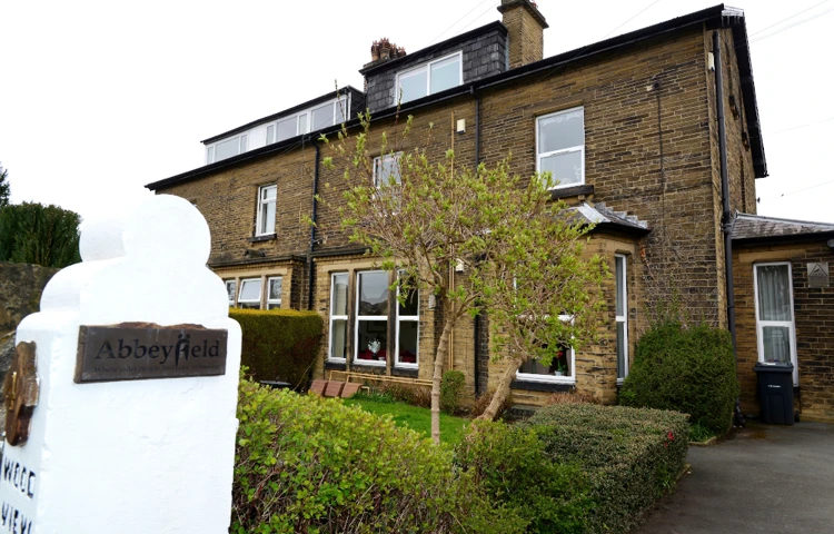 A white post with an Abbeyfield sign and the house in the background