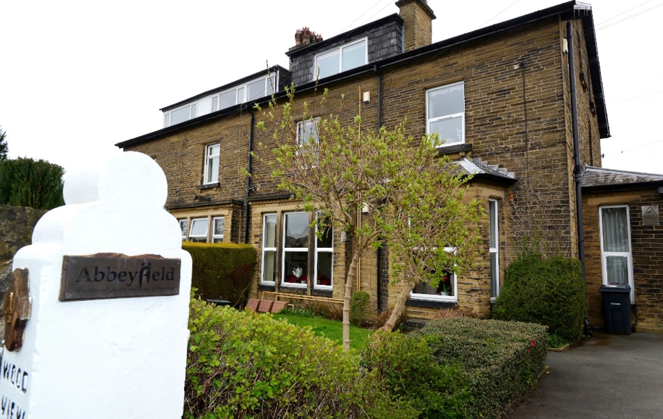A white post with an Abbeyfield sign and the house in the background