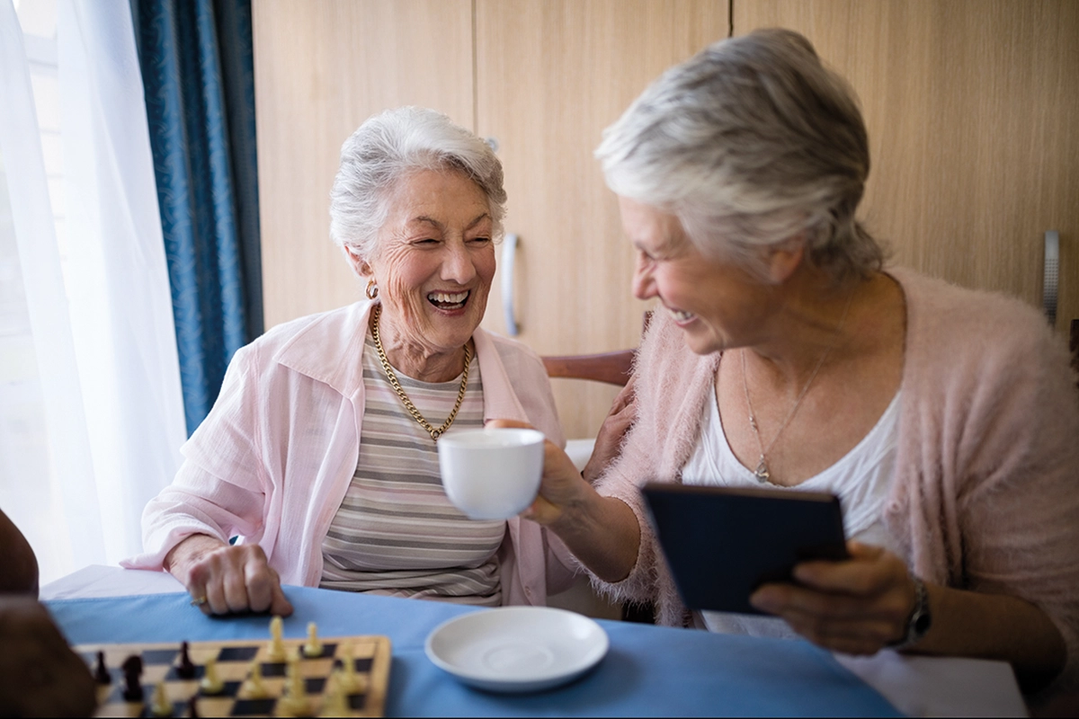 Two Smiling Older Women Enjoying A Game Of Chess And A Tea