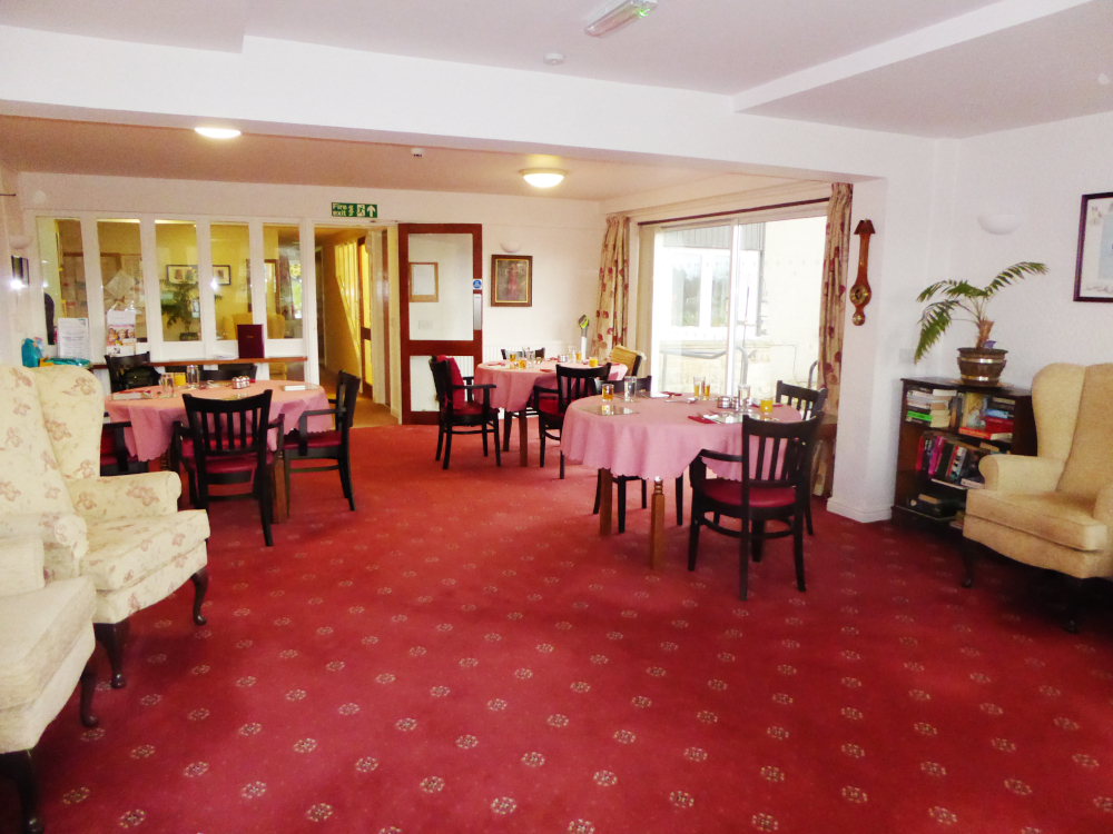 Bright dining area with red carpet and round tables at Abbeyfield House sheltered housing in North Yorkshire