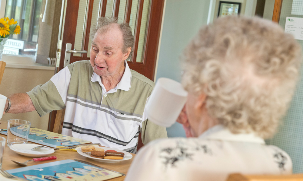 Residents are sat at the table enjoying tea and biscuits