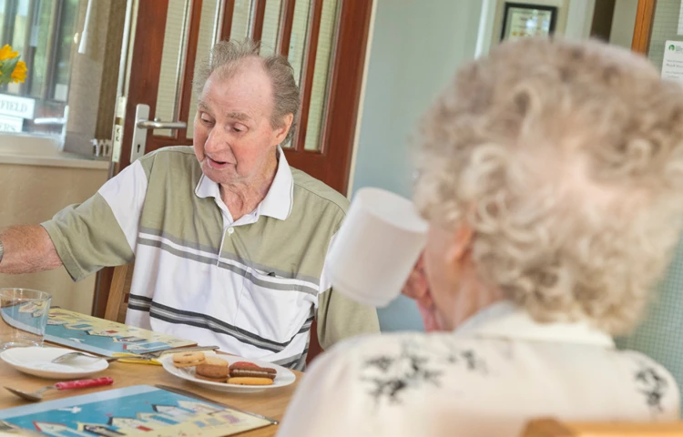 Residents are sat at the table enjoying tea and biscuits