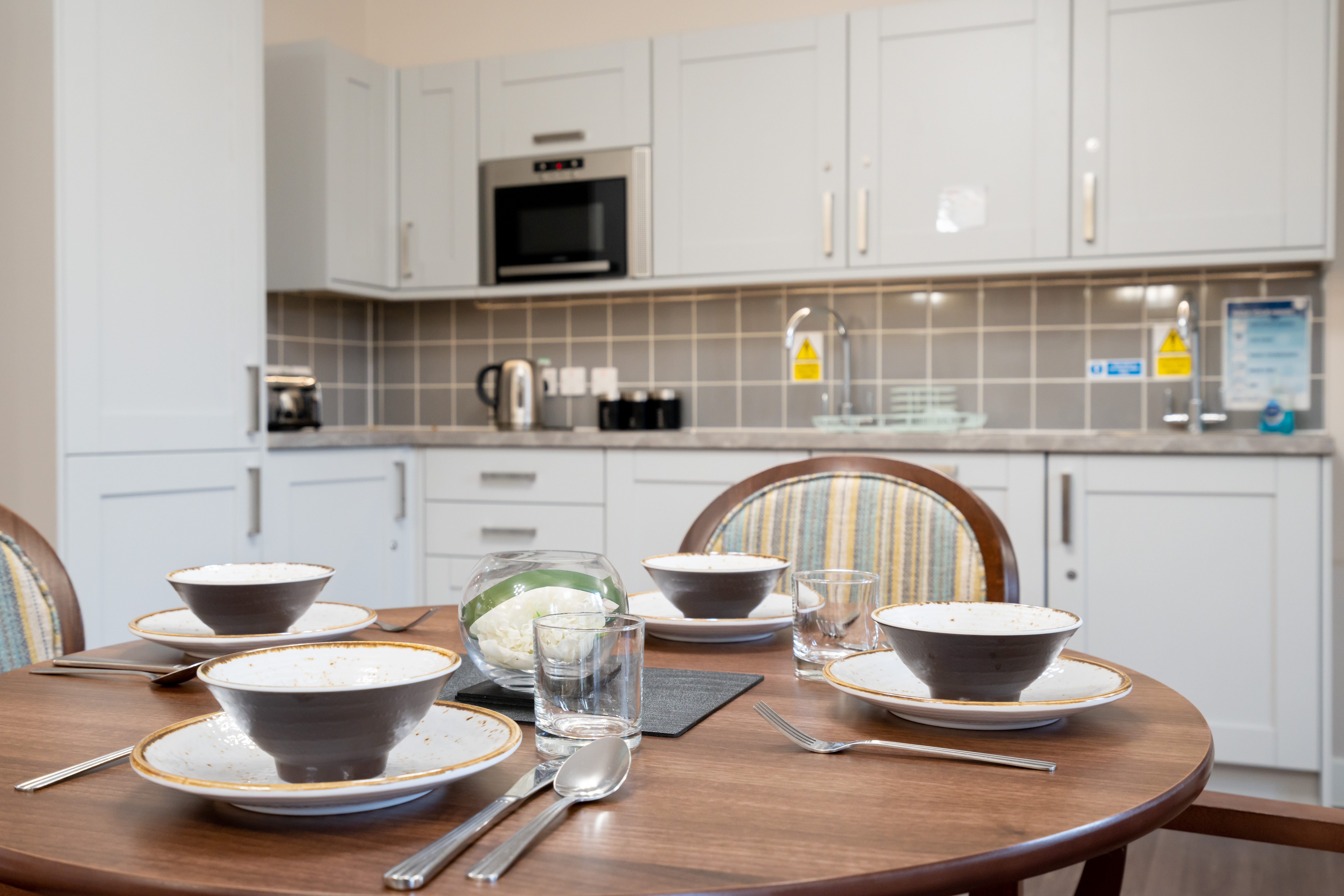 Dining table set for a meal in a modern dining room at Westall House, with kitchen cabinets in the background